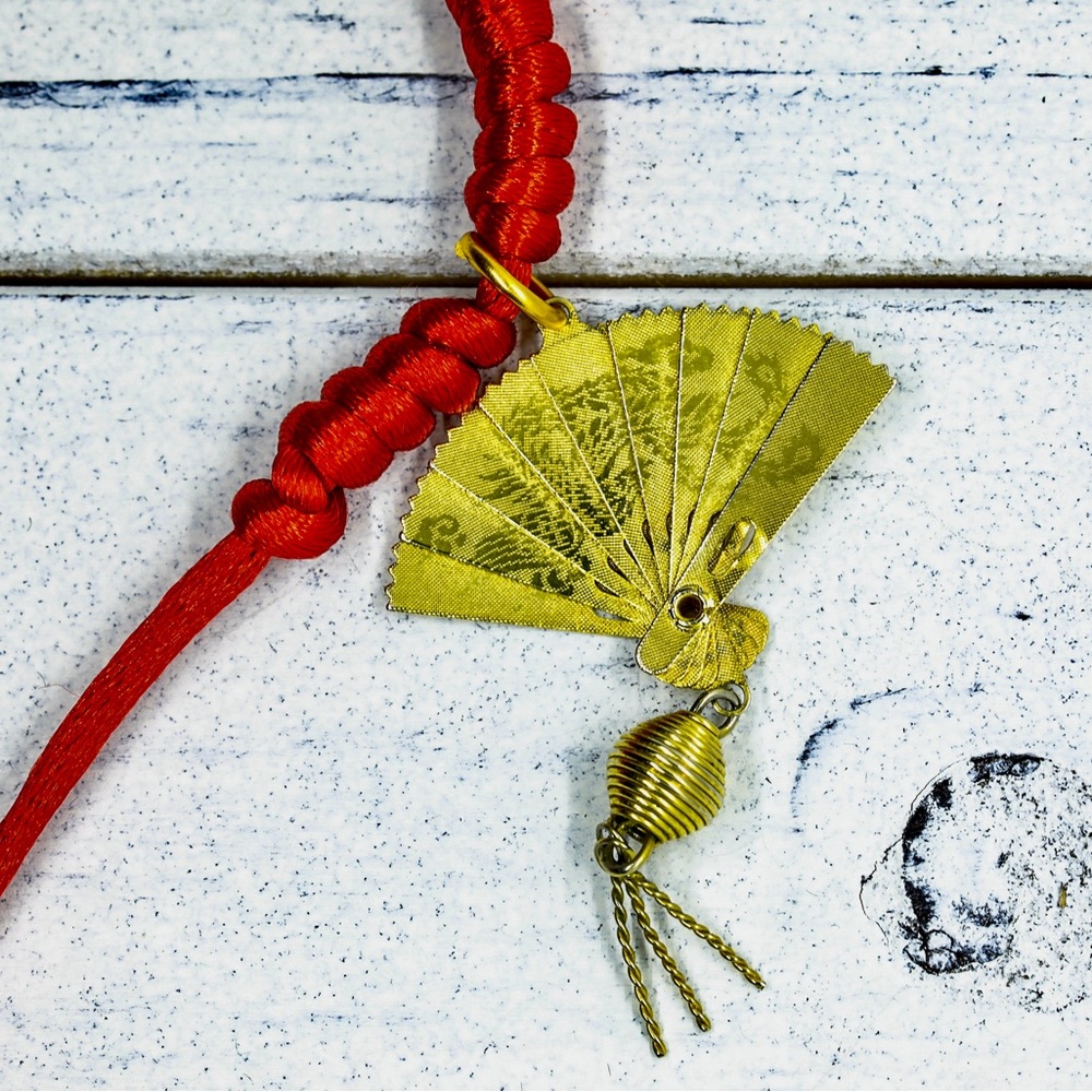 Gold plated fan pendant on a red knotted satin cord.